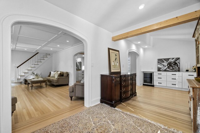 hallway featuring arched walkways, wine cooler, stairs, light wood-type flooring, and beam ceiling