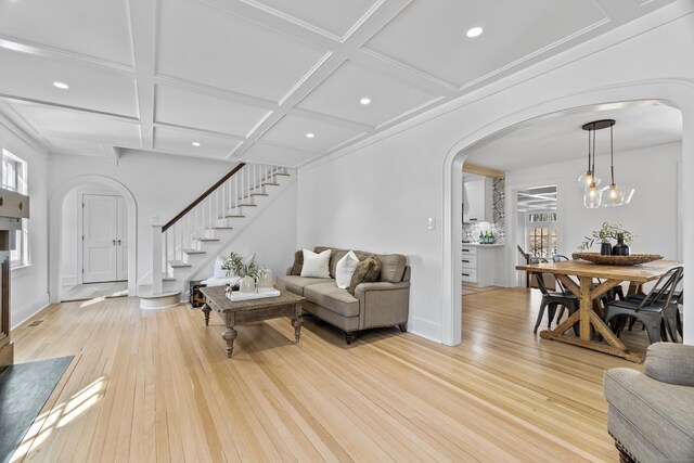 living area featuring arched walkways, stairway, light wood-type flooring, coffered ceiling, and baseboards