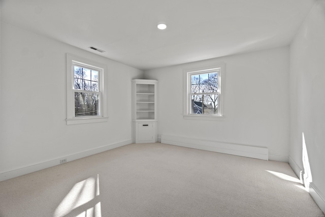 carpeted spare room featuring a baseboard heating unit, plenty of natural light, visible vents, and baseboards