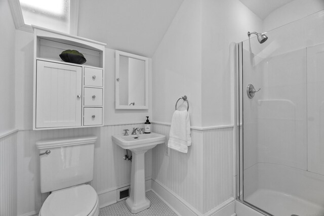 bathroom with toilet, a wainscoted wall, a shower with door, and a sink