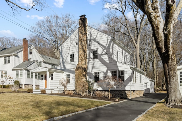 view of front facade featuring driveway, a chimney, and a front yard