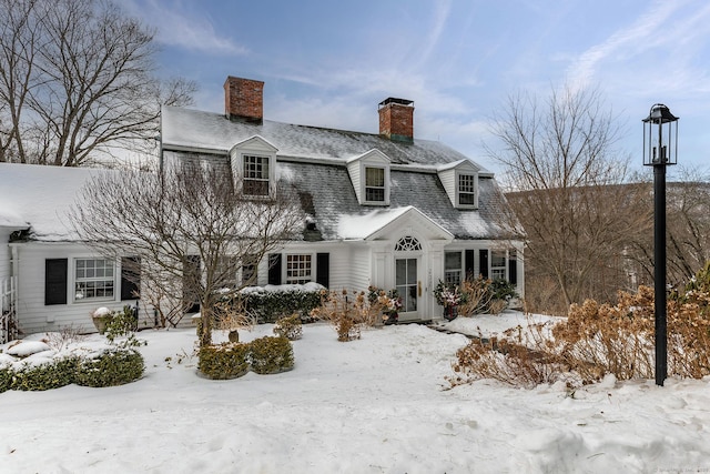 view of front facade featuring roof with shingles, a chimney, and a gambrel roof