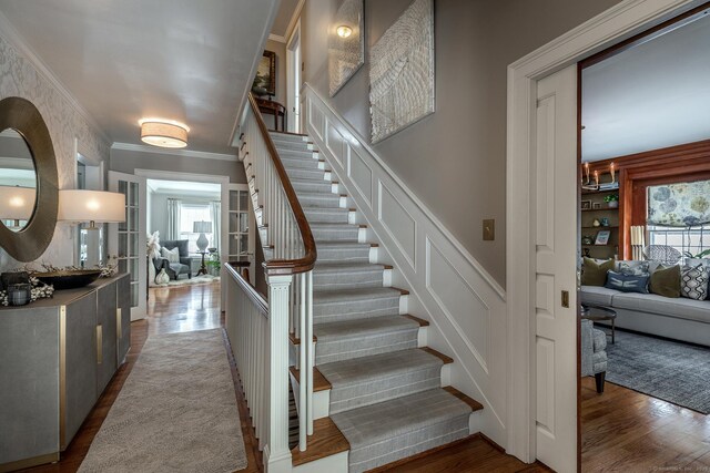 stairs featuring a decorative wall, wood finished floors, and crown molding