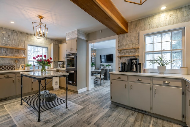 kitchen with light countertops, light wood-type flooring, open shelves, multiple ovens, and pendant lighting