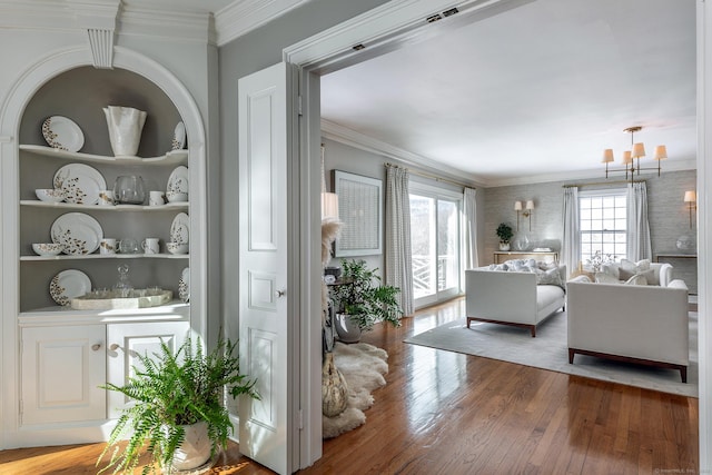 living room featuring built in shelves, wood-type flooring, an inviting chandelier, and crown molding