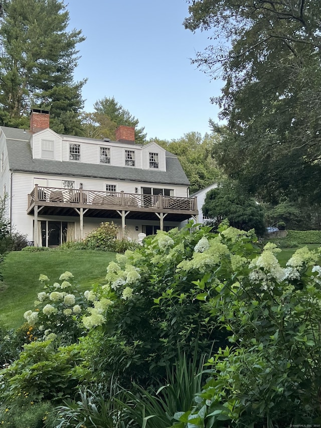 rear view of property featuring a chimney, a deck, and a lawn