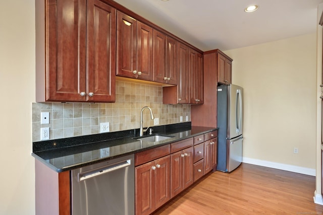 kitchen featuring light hardwood / wood-style flooring, sink, dark stone counters, stainless steel appliances, and decorative backsplash