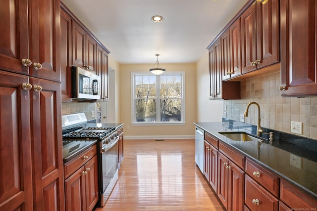 kitchen featuring dark stone countertops, sink, light wood-type flooring, pendant lighting, and stainless steel appliances