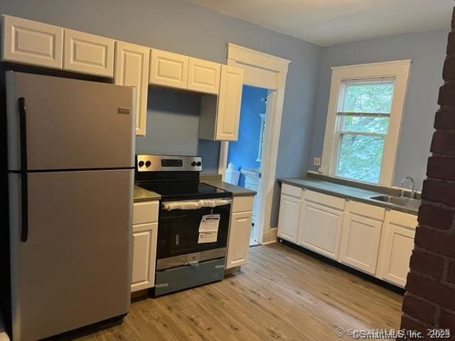 kitchen with light wood finished floors, appliances with stainless steel finishes, a sink, and white cabinetry