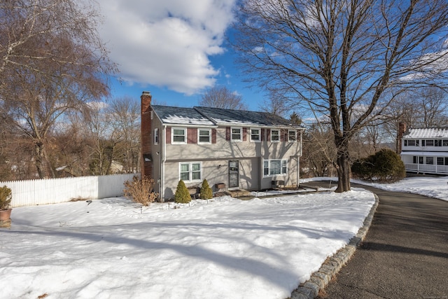 colonial-style house featuring a chimney and fence