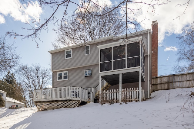 snow covered back of property with a sunroom, a chimney, stairway, fence, and a wooden deck