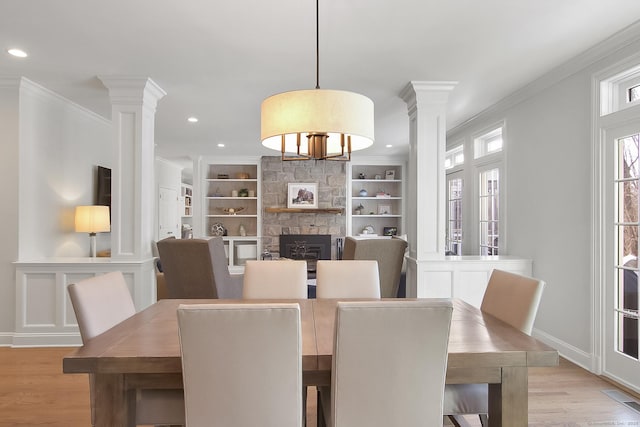 dining area with a fireplace, ornamental molding, light wood-type flooring, and ornate columns