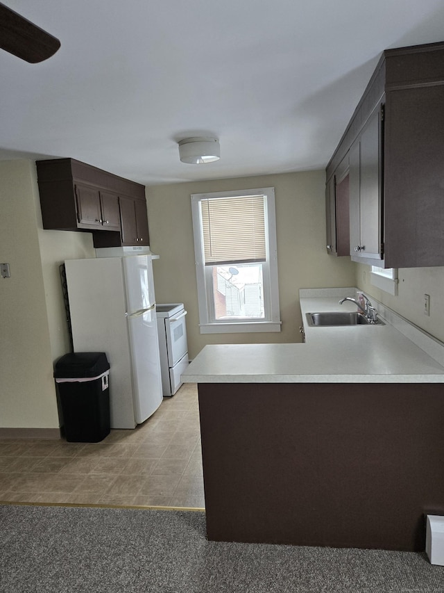 kitchen featuring light countertops, a sink, dark brown cabinetry, white appliances, and a peninsula