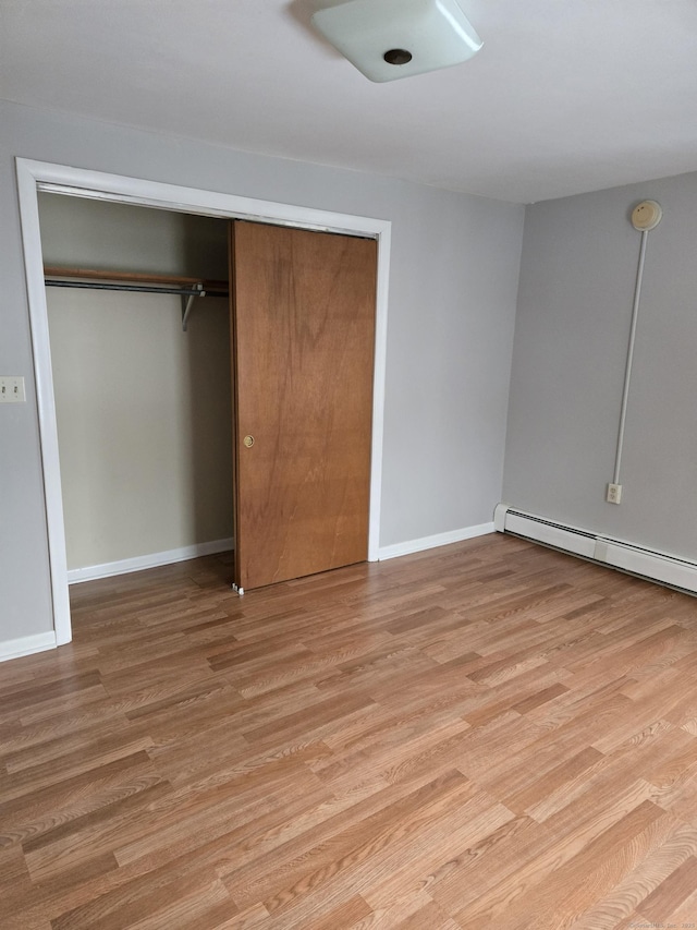 unfurnished bedroom featuring light wood-style floors, baseboards, and a baseboard heating unit