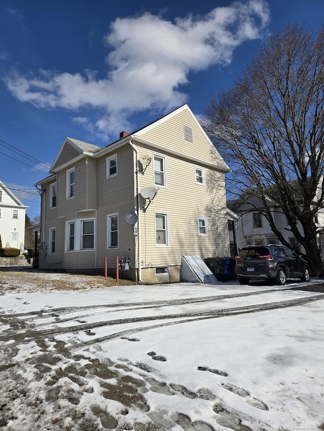 snow covered rear of property featuring a chimney