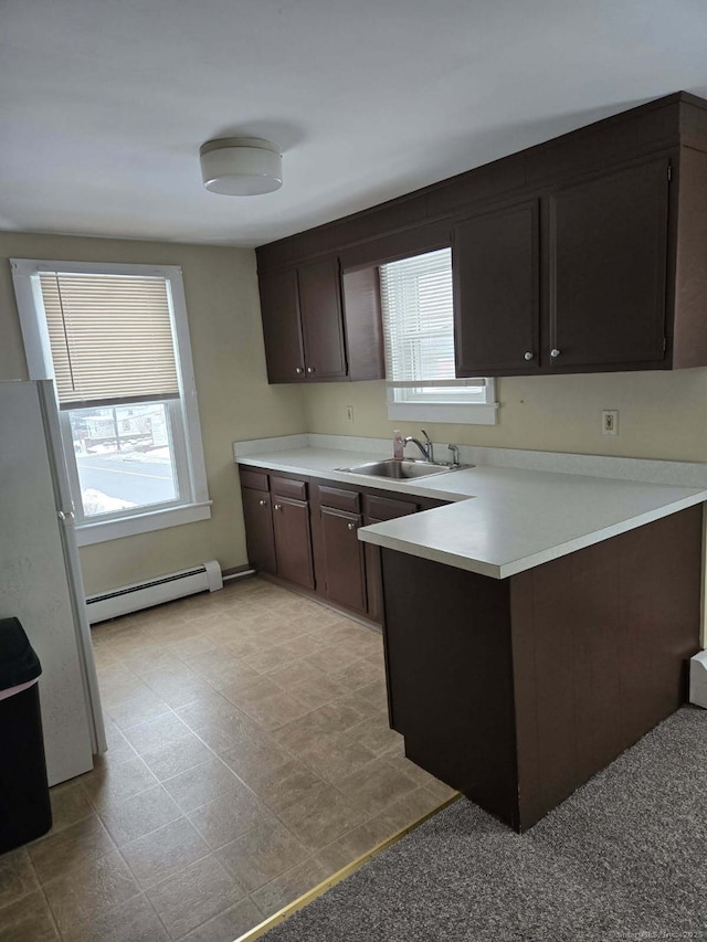 kitchen with light countertops, baseboard heating, freestanding refrigerator, a sink, and a peninsula