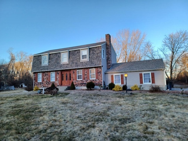 dutch colonial featuring a front lawn, a chimney, and a shingled roof