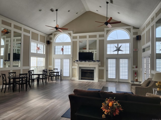 living room with a healthy amount of sunlight, high vaulted ceiling, wood finished floors, and a glass covered fireplace