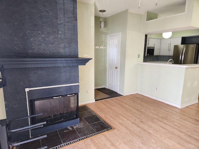 unfurnished living room with a sink, wood finished floors, a multi sided fireplace, and baseboards