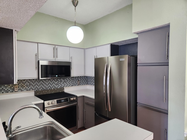 kitchen featuring a sink, white cabinets, light countertops, appliances with stainless steel finishes, and hanging light fixtures