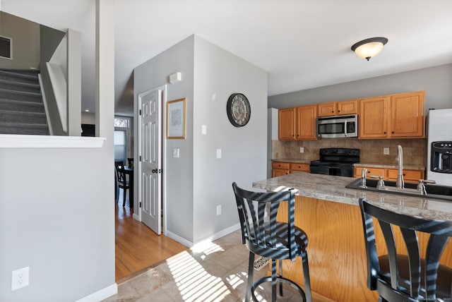 kitchen featuring sink, a kitchen breakfast bar, black electric range oven, kitchen peninsula, and decorative backsplash