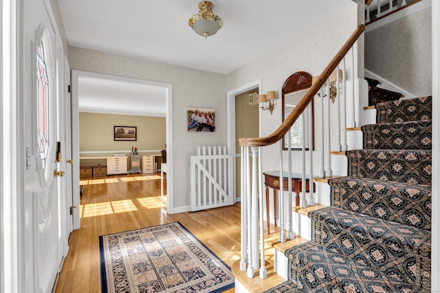 entryway featuring wallpapered walls, light wood-style flooring, baseboards, and stairs