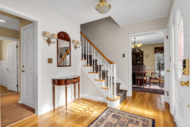 foyer entrance with stairway, wood finished floors, and a notable chandelier