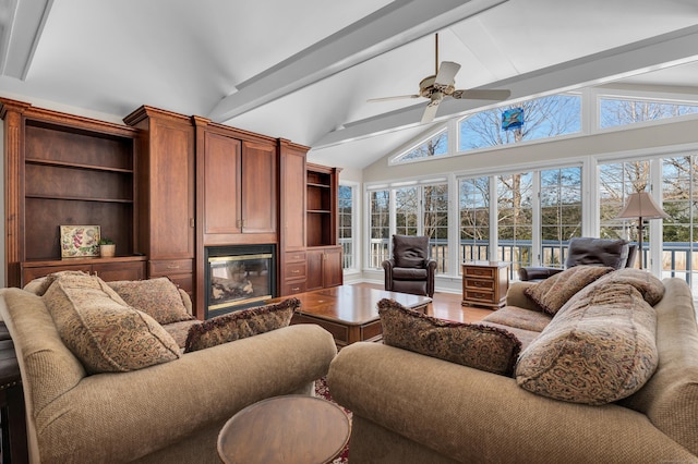 living area featuring ceiling fan, beam ceiling, wood finished floors, and a glass covered fireplace