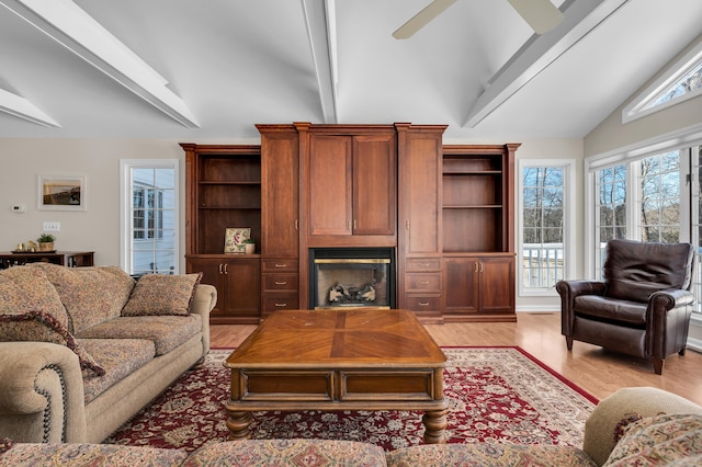 living area with light wood finished floors, a fireplace, high vaulted ceiling, and a ceiling fan