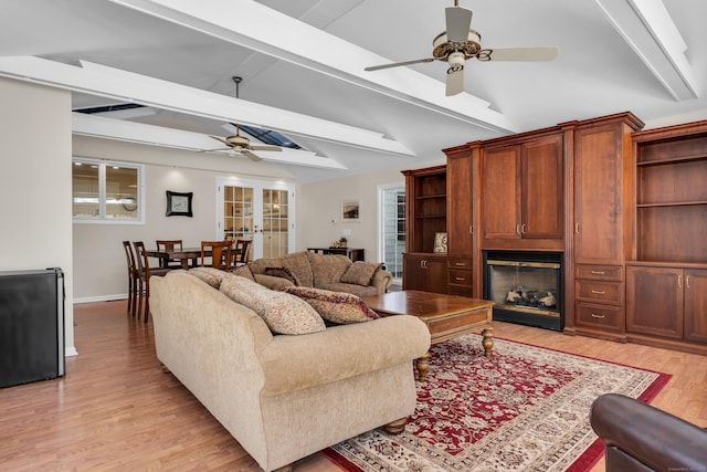 living room featuring vaulted ceiling with beams, light wood-style flooring, a fireplace, a ceiling fan, and baseboards