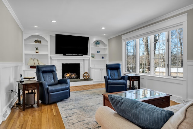 living room with built in shelves, a brick fireplace, a wainscoted wall, and ornamental molding