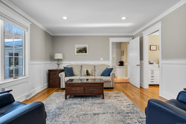 living room featuring light wood finished floors, ornamental molding, and a wainscoted wall