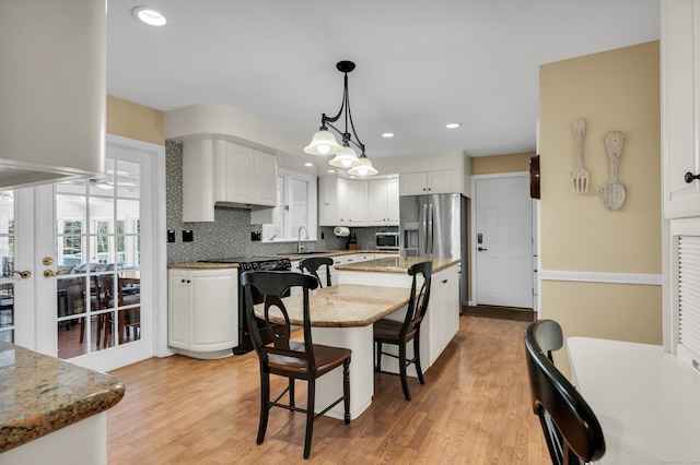 kitchen with a sink, a kitchen island, white cabinetry, appliances with stainless steel finishes, and pendant lighting