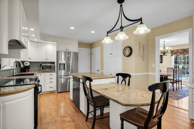 kitchen with light stone counters, a center island, pendant lighting, stainless steel appliances, and white cabinetry