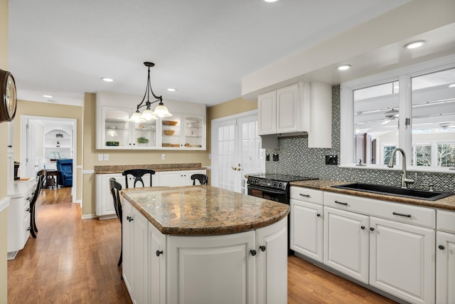 kitchen featuring glass insert cabinets, a sink, a kitchen island, white cabinets, and decorative light fixtures