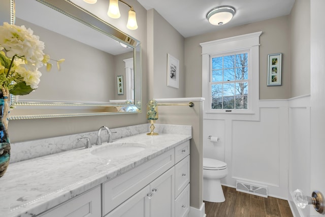 bathroom with visible vents, wainscoting, toilet, wood finished floors, and vanity