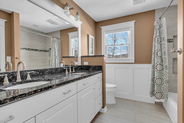 full bathroom featuring a wainscoted wall, double vanity, a sink, and toilet