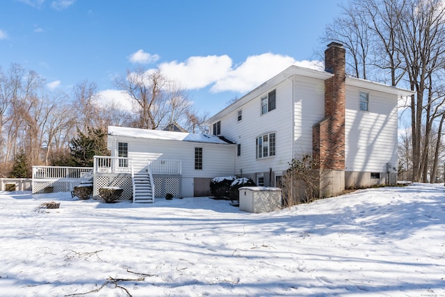 snow covered house with a deck, stairway, and a chimney