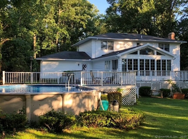 rear view of house with a yard, a chimney, a wooden deck, and an outdoor pool