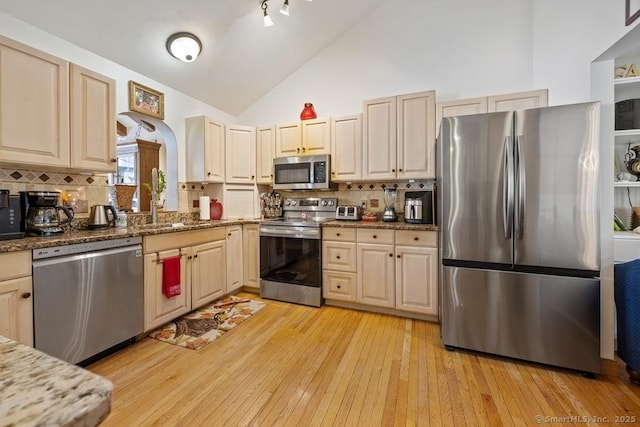 kitchen featuring dark stone counters, decorative backsplash, light wood-style flooring, stainless steel appliances, and high vaulted ceiling