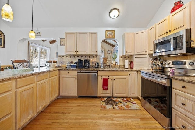 kitchen with stainless steel appliances, light brown cabinets, hanging light fixtures, and a sink