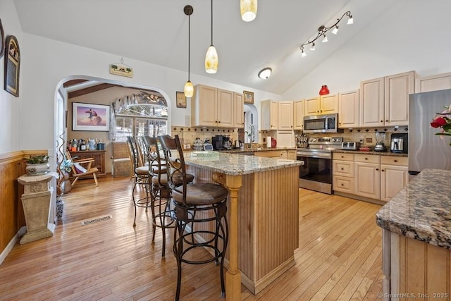 kitchen with stainless steel appliances, light brown cabinets, decorative light fixtures, and dark stone countertops