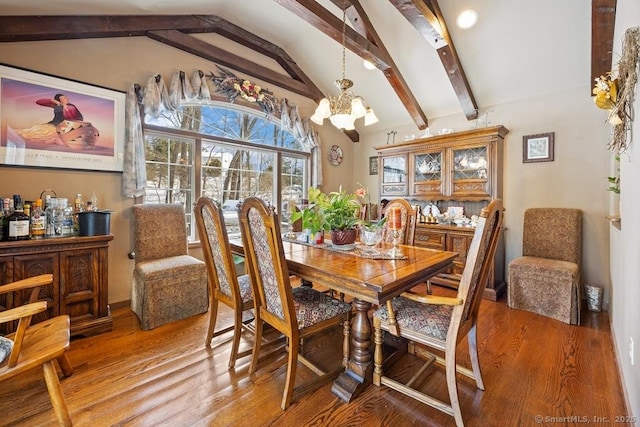 dining room featuring lofted ceiling with beams, a notable chandelier, and wood finished floors