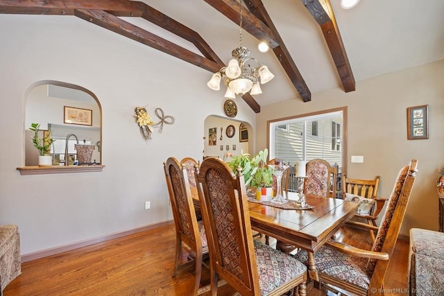 dining area featuring lofted ceiling with beams, light wood finished floors, arched walkways, and an inviting chandelier