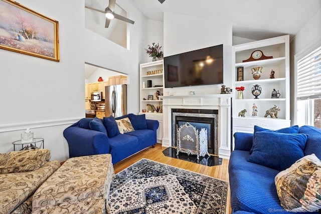 living room with ceiling fan, high vaulted ceiling, a premium fireplace, and light wood-style floors