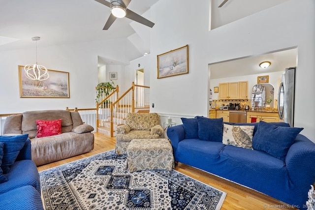 living room with light wood-type flooring, ceiling fan, stairs, and high vaulted ceiling