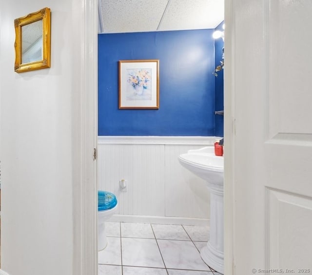 half bath with a drop ceiling, wainscoting, toilet, and tile patterned floors