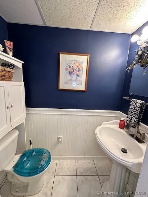 half bath featuring tile patterned flooring, wainscoting, toilet, and a drop ceiling