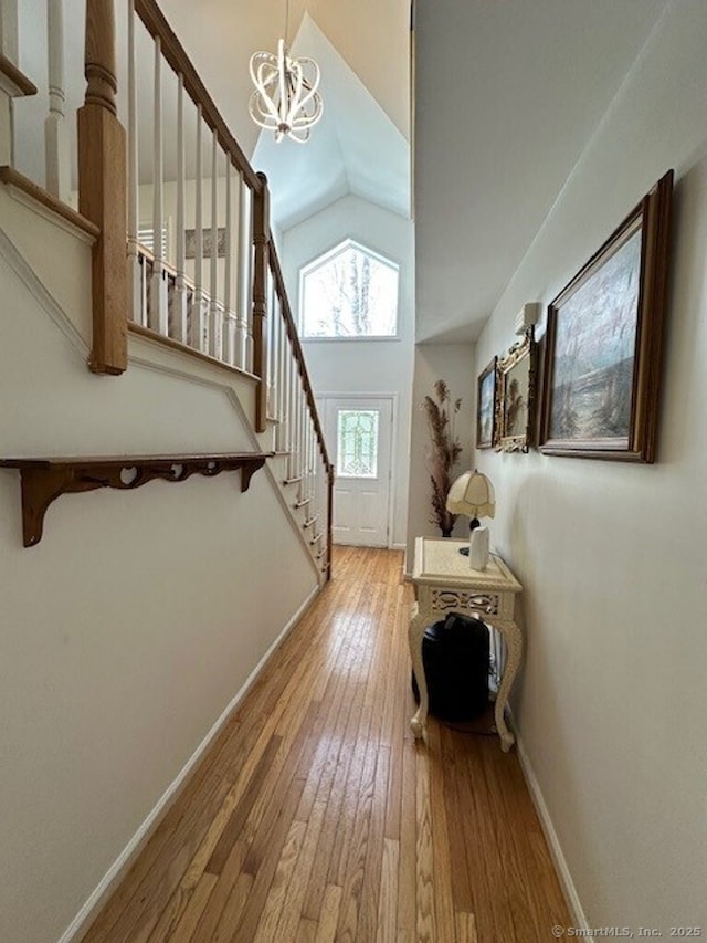 foyer entrance featuring lofted ceiling, stairway, wood finished floors, a chandelier, and baseboards