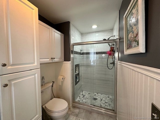 bathroom featuring a wainscoted wall, a stall shower, and toilet